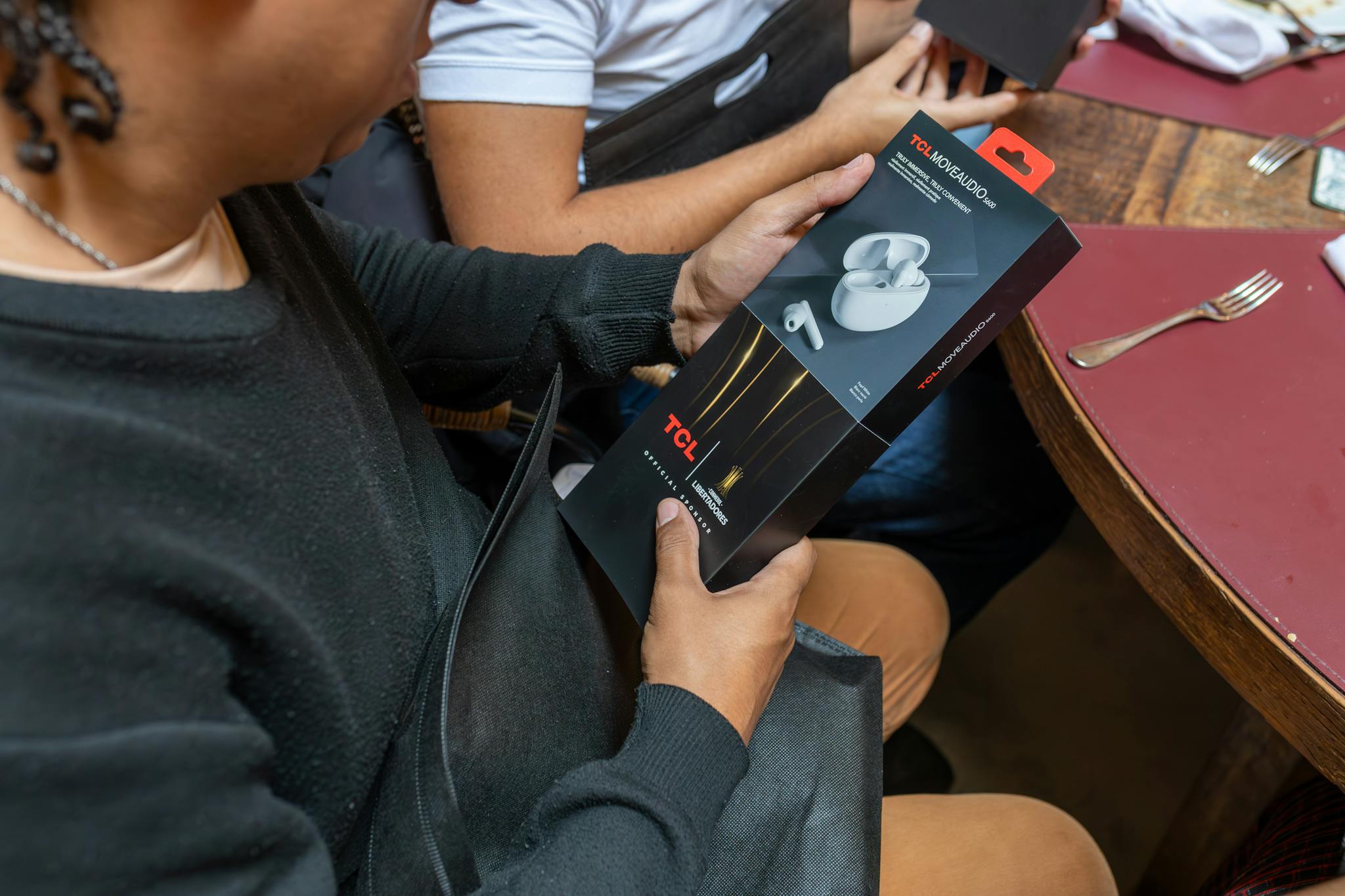 Person holding a TCL wireless earphone box, showcasing modern technology indoors.