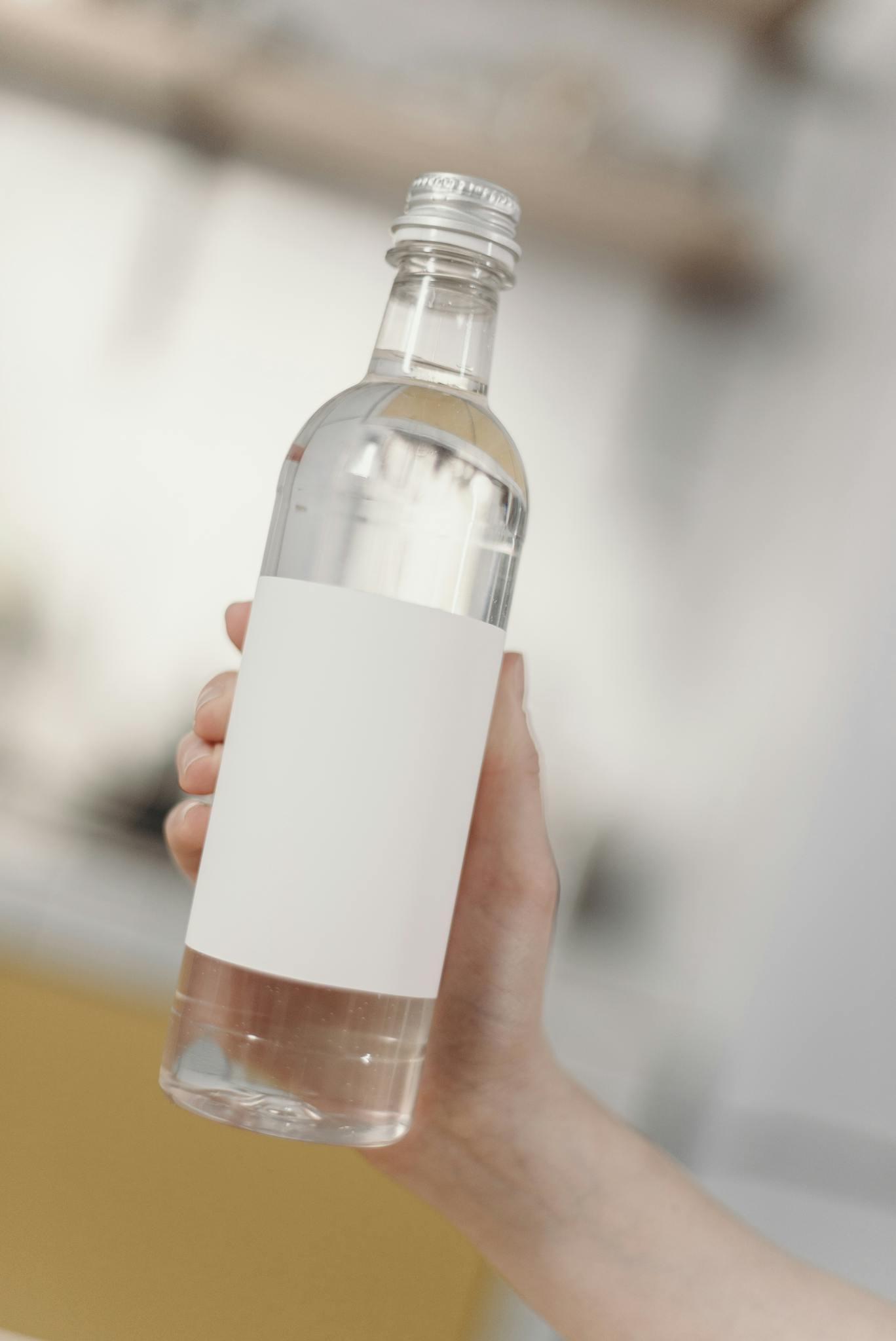 Clear bottle held by a hand with blank label for branding mockup. Minimalist design with a soft focus background.
