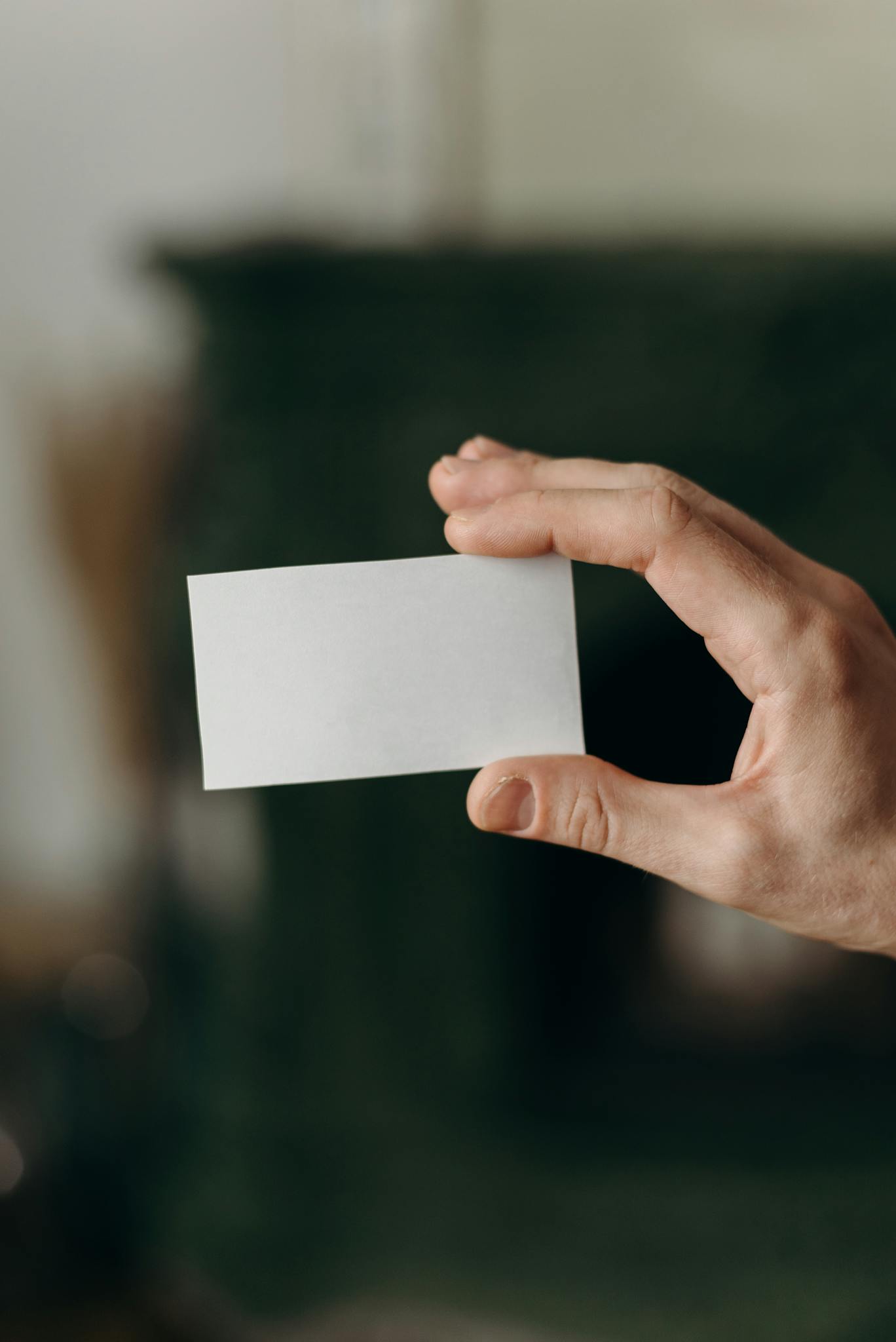 Close-up of a hand holding a blank white card with blurred background, perfect for business presentations and mockups.